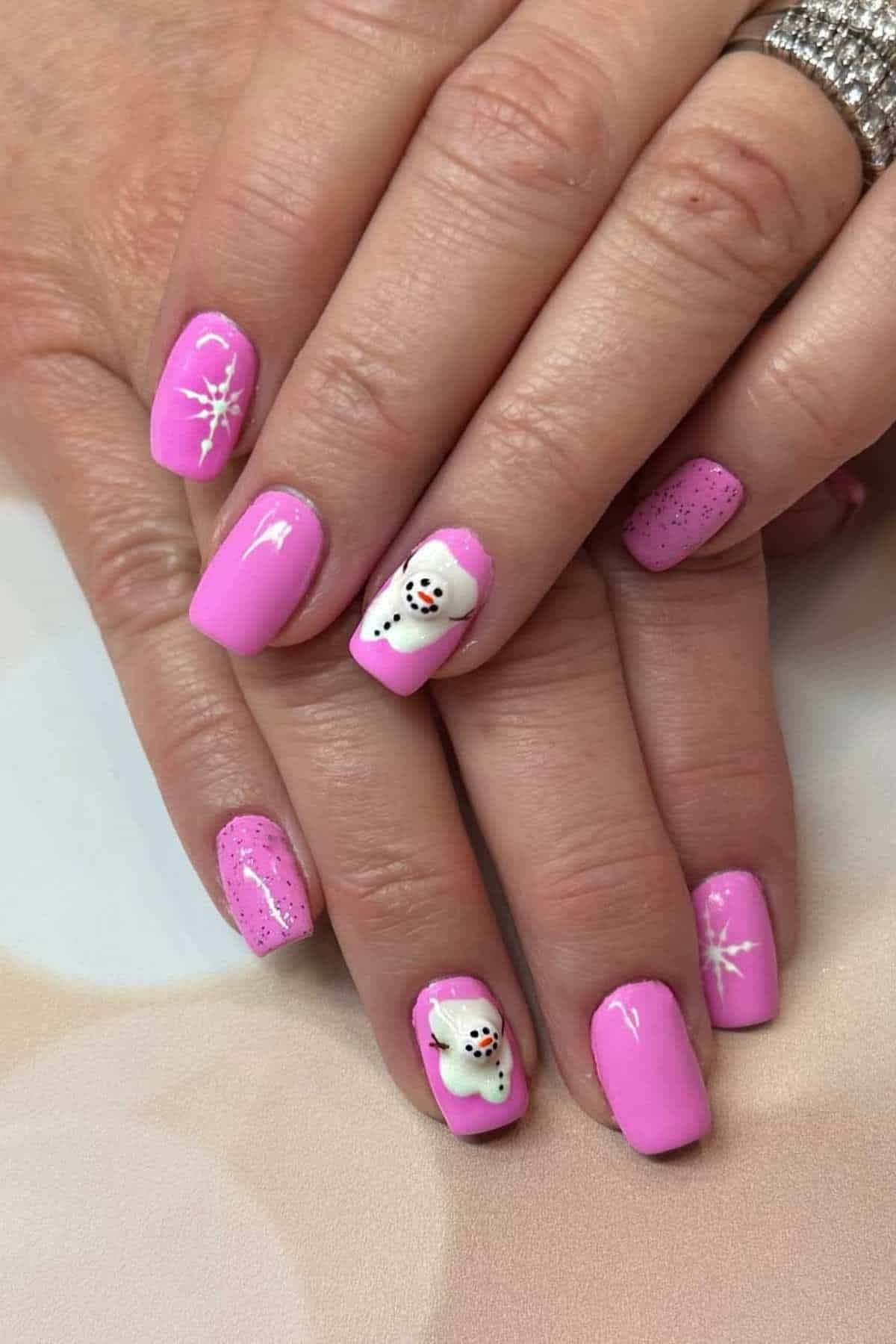 Hands with pink manicured nails, snowflake designs on some nails, and snowman art on ring fingernails.