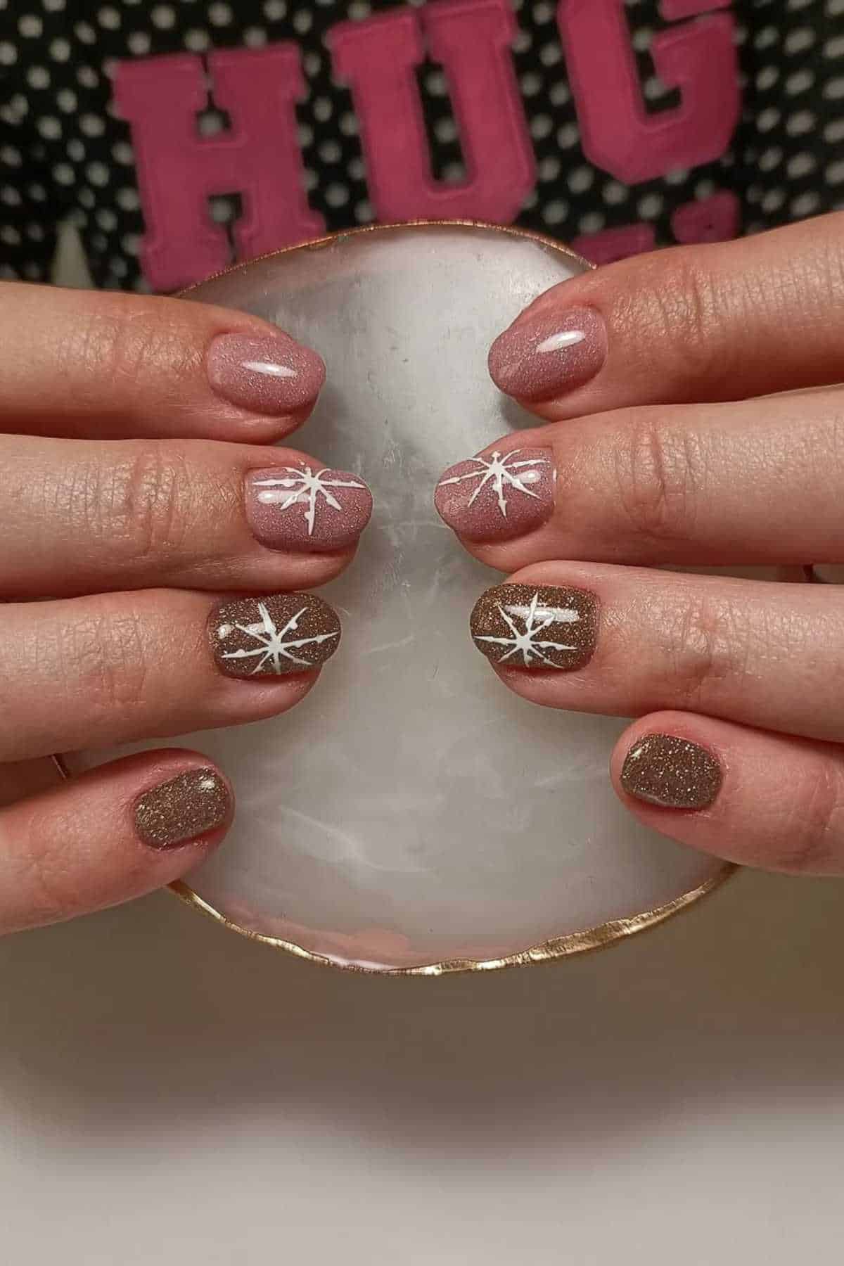 Hands with manicured nails featuring pink and gold glitter polish, some with white star designs, holding a round, translucent stone.