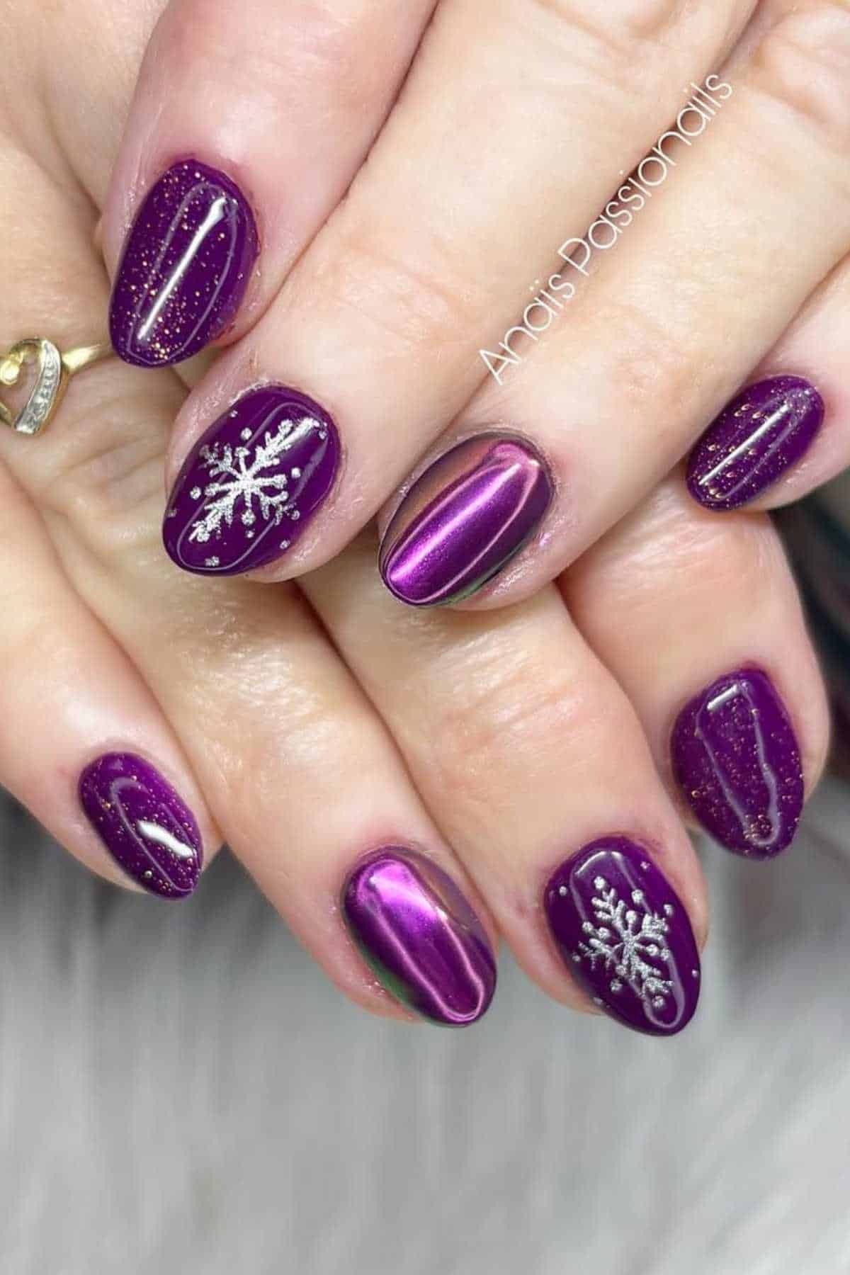 Hands with purple glossy manicure; some nails feature silver snowflake designs and fine glitter accents.