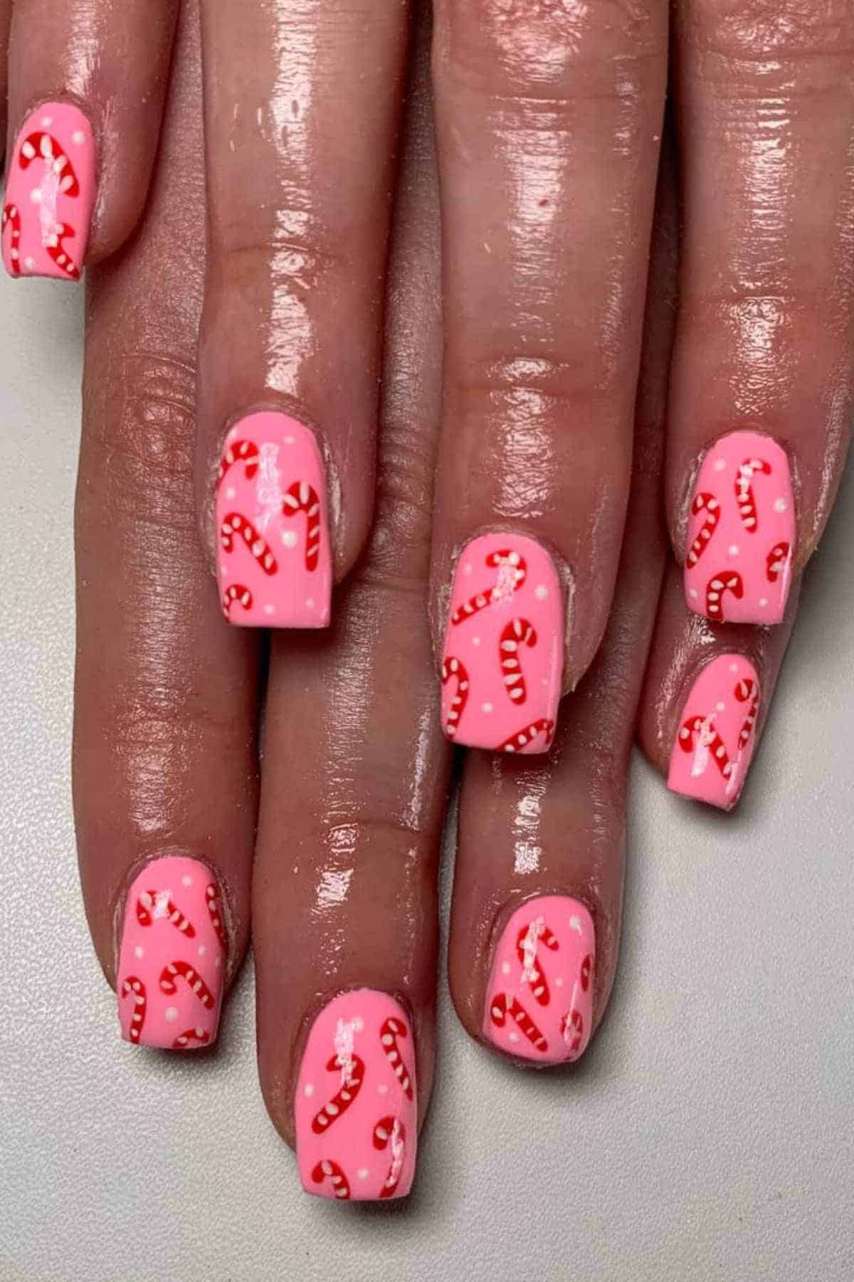Close-up of hands with pink nail polish and red and white candy cane designs on each fingernail.