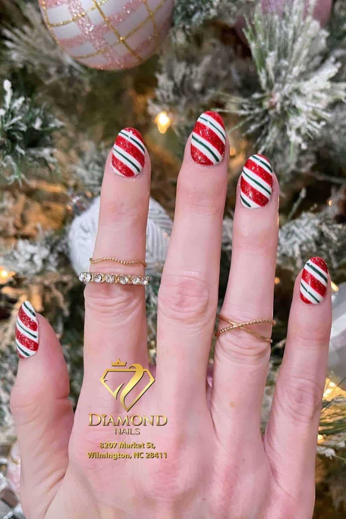 A hand with red, white, and green striped Christmas-themed nail art is shown near a decorated Christmas tree. The image also displays Diamond Nails’ logo and address.