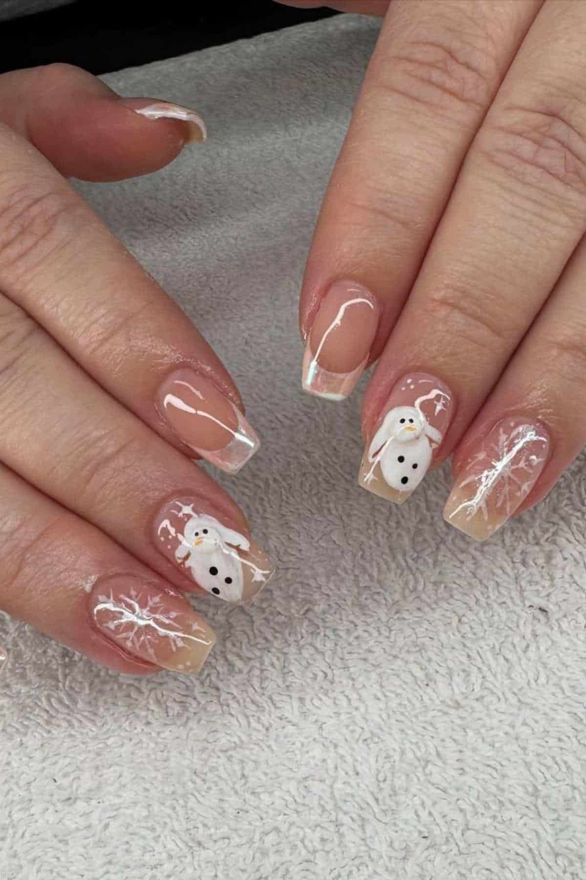 Hands with clear French tip manicures featuring white snowflake designs and snowman nail art on a light textured surface.