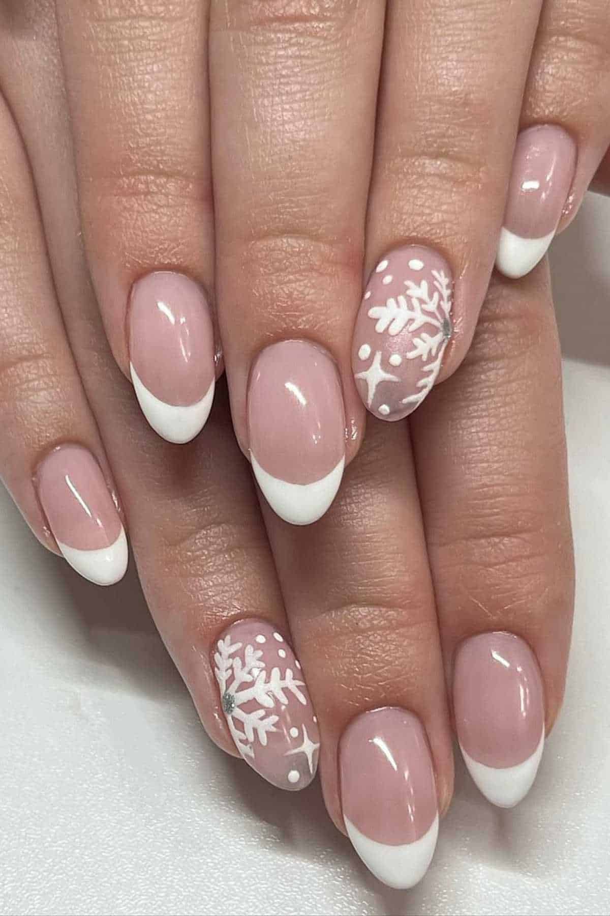 Hands with a French manicure featuring white tips and snowflake designs on two accent nails, set against a plain background.