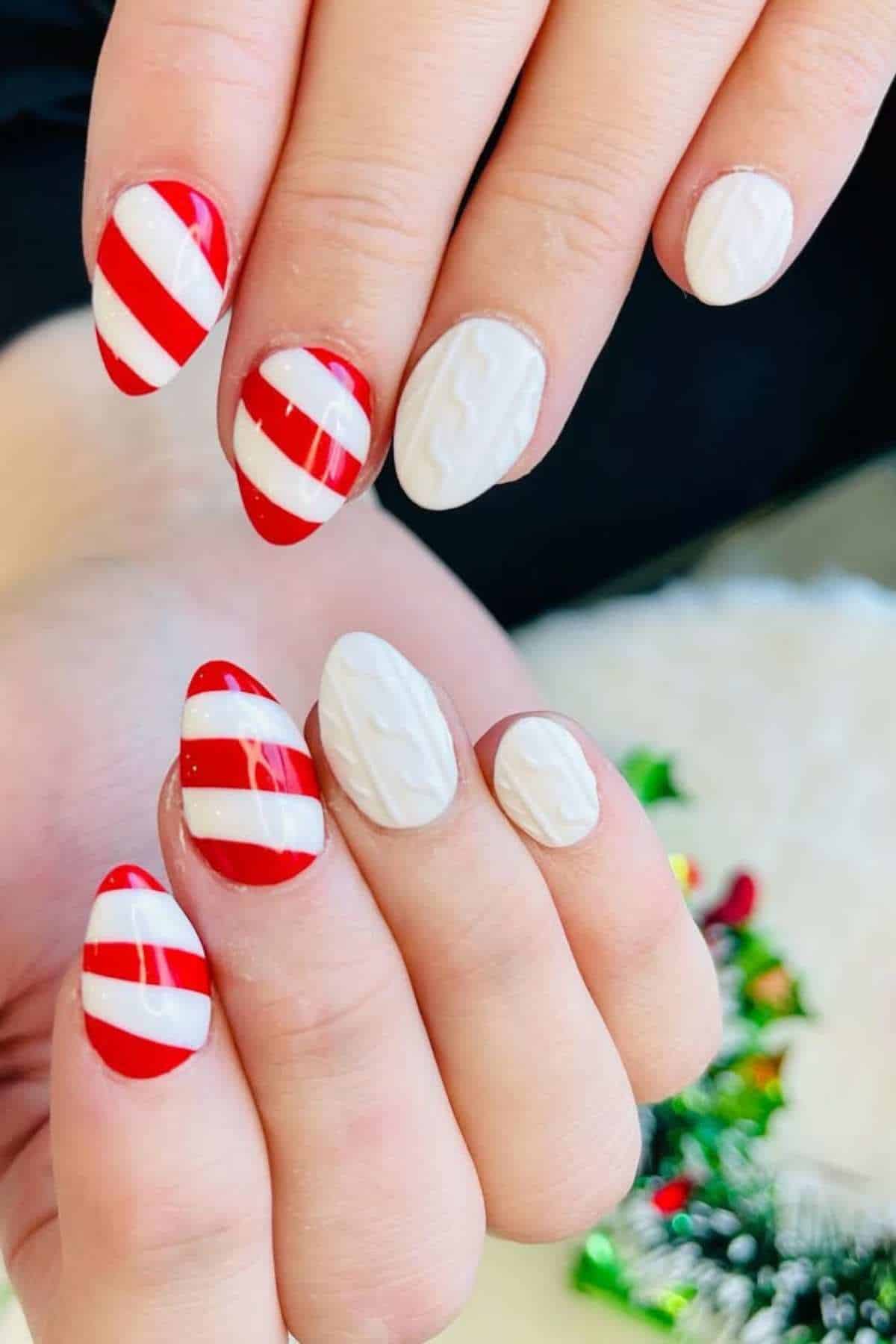Hands with almond-shaped nails featuring red and white diagonal stripes on some nails and solid white nails with a raised cable knit texture on others.