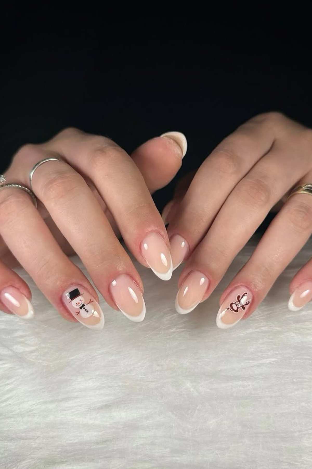 Hands with almond-shaped French manicure, featuring minimalist black and white snowman designs on the ring fingers, resting on a white textured surface.