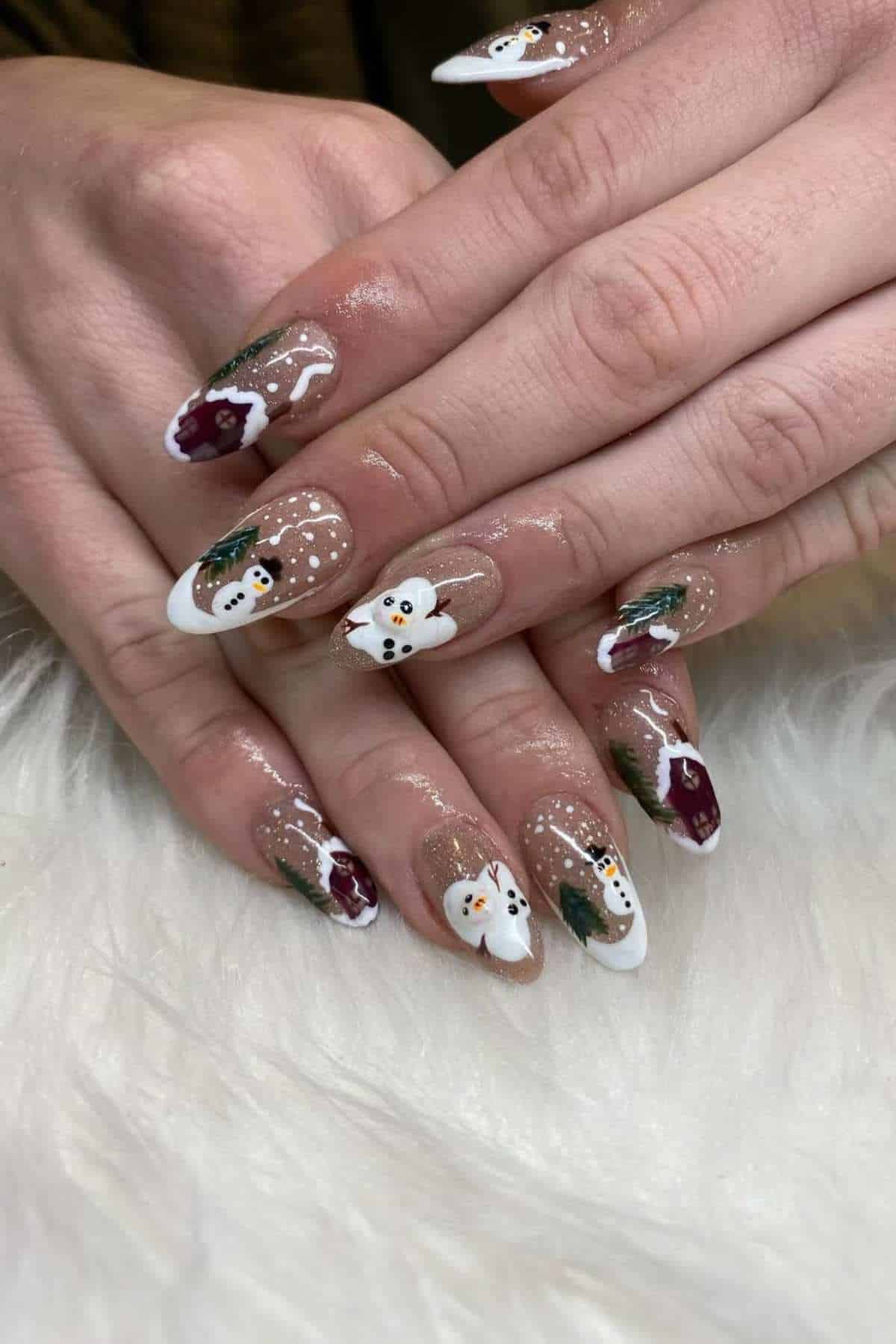 Hands with almond-shaped nails featuring winter-themed nail art, including snowmen, pine trees, and white tips, on a fuzzy white surface.