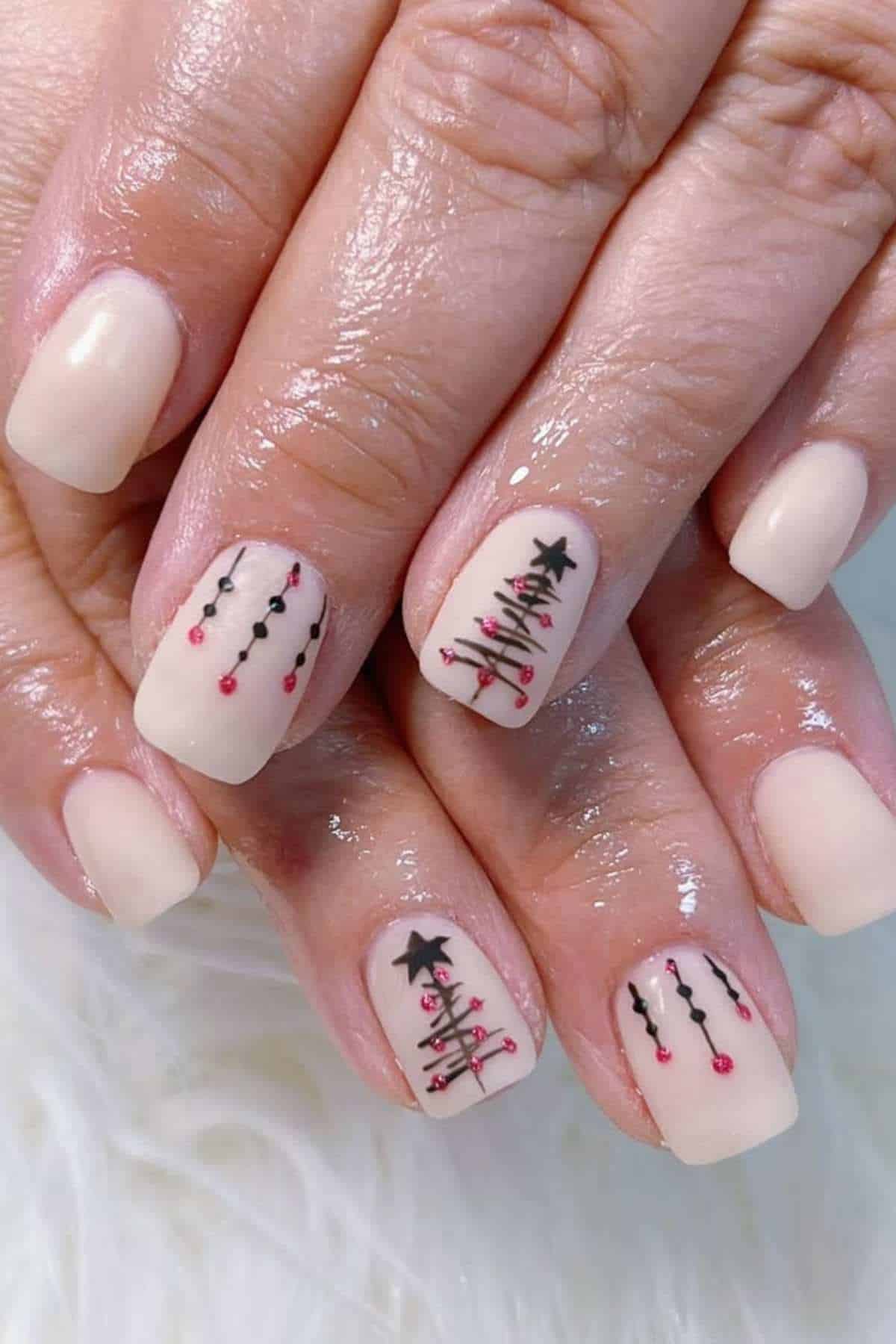 Close-up of hands with nude-colored nail polish, featuring Christmas tree and ornament designs in black and red on two accent nails.