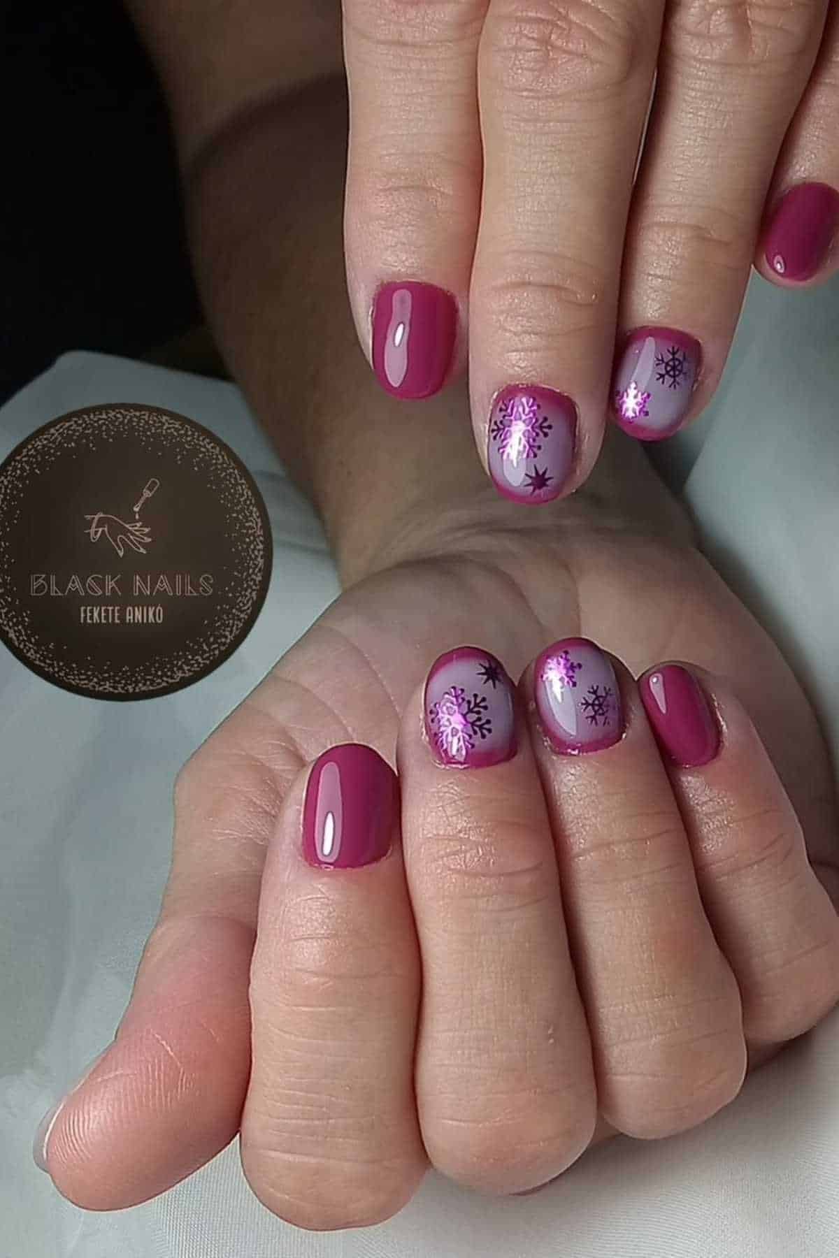 Close-up of hands with short, glossy purple nails; some nails feature light purple accents with dark purple snowflake designs.