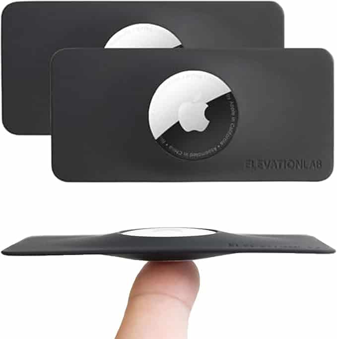 Two black rectangular holders, each displaying an Apple AirTag in the center; one is balanced on a fingertip, showing its slim profile.