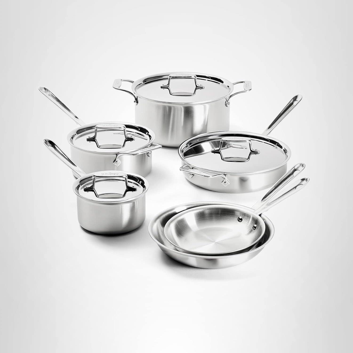 A set of stainless steel pots and pans with lids, arranged on a white background.
