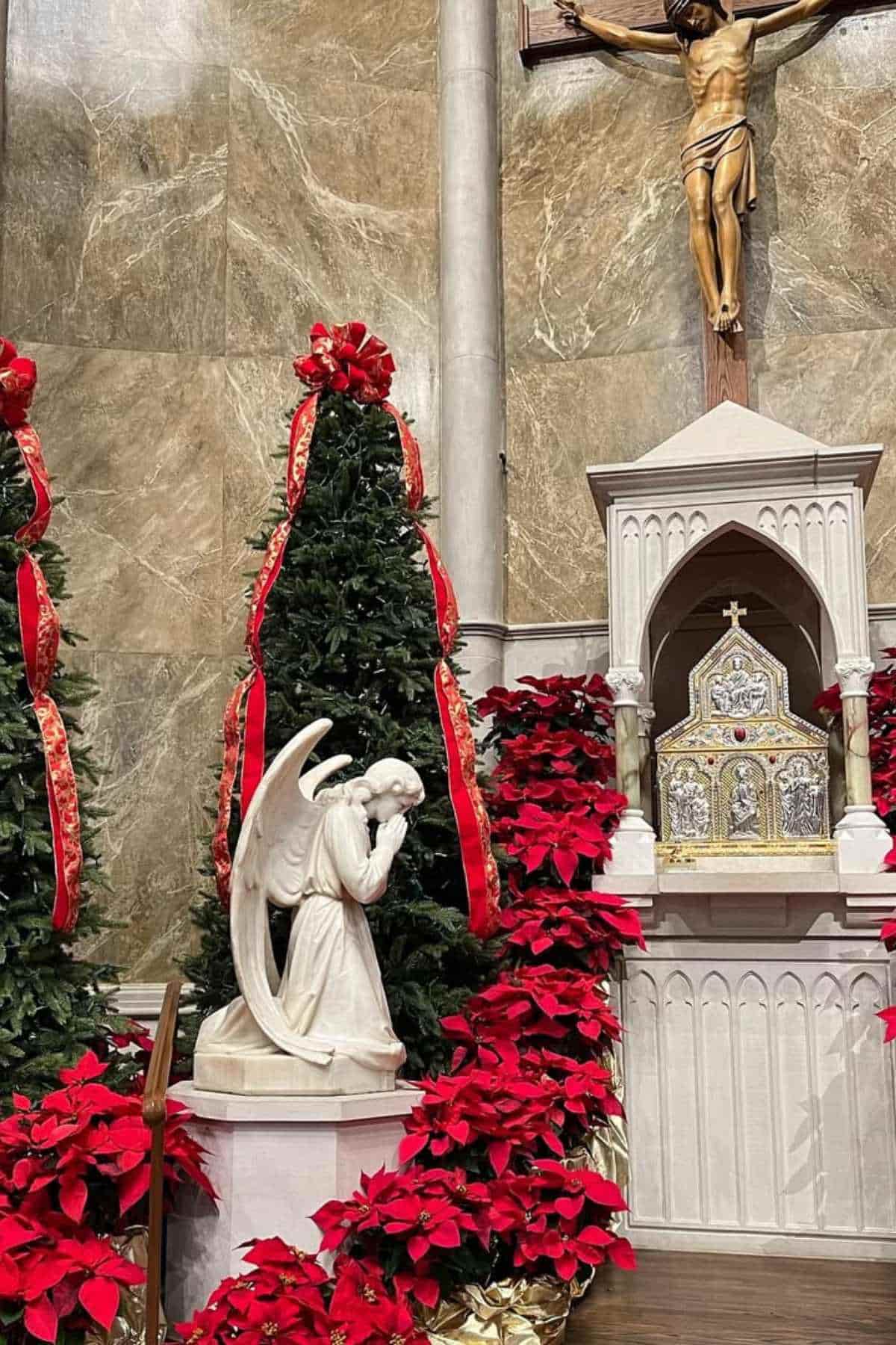 Church altar decorated with red poinsettias, Christmas trees with red bows, a white angel statue, and a crucifix on the wall.