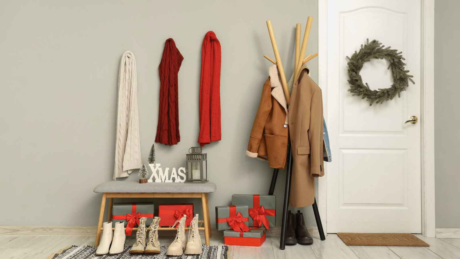 Entryway with winter coats, scarves, boots, wrapped gifts, and Christmas decorations including a wreath on the door and an "XMAS" sign on a bench.