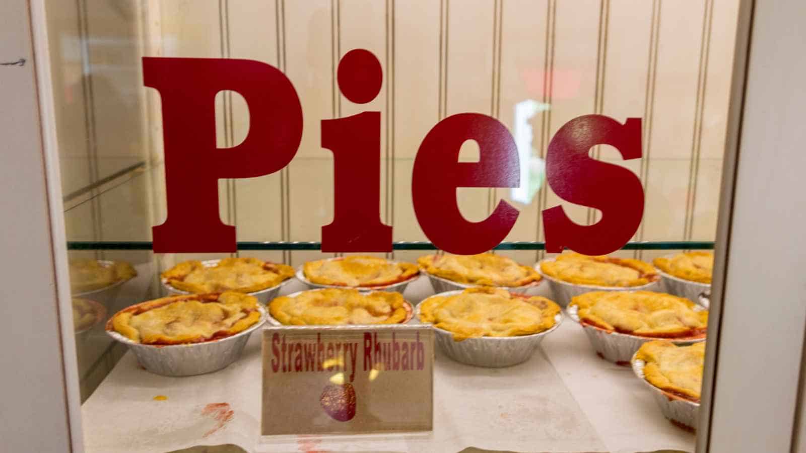 Several small pies are displayed on a shelf behind glass with the word "Pies" and a label that reads "Strawberry Rhubarb.