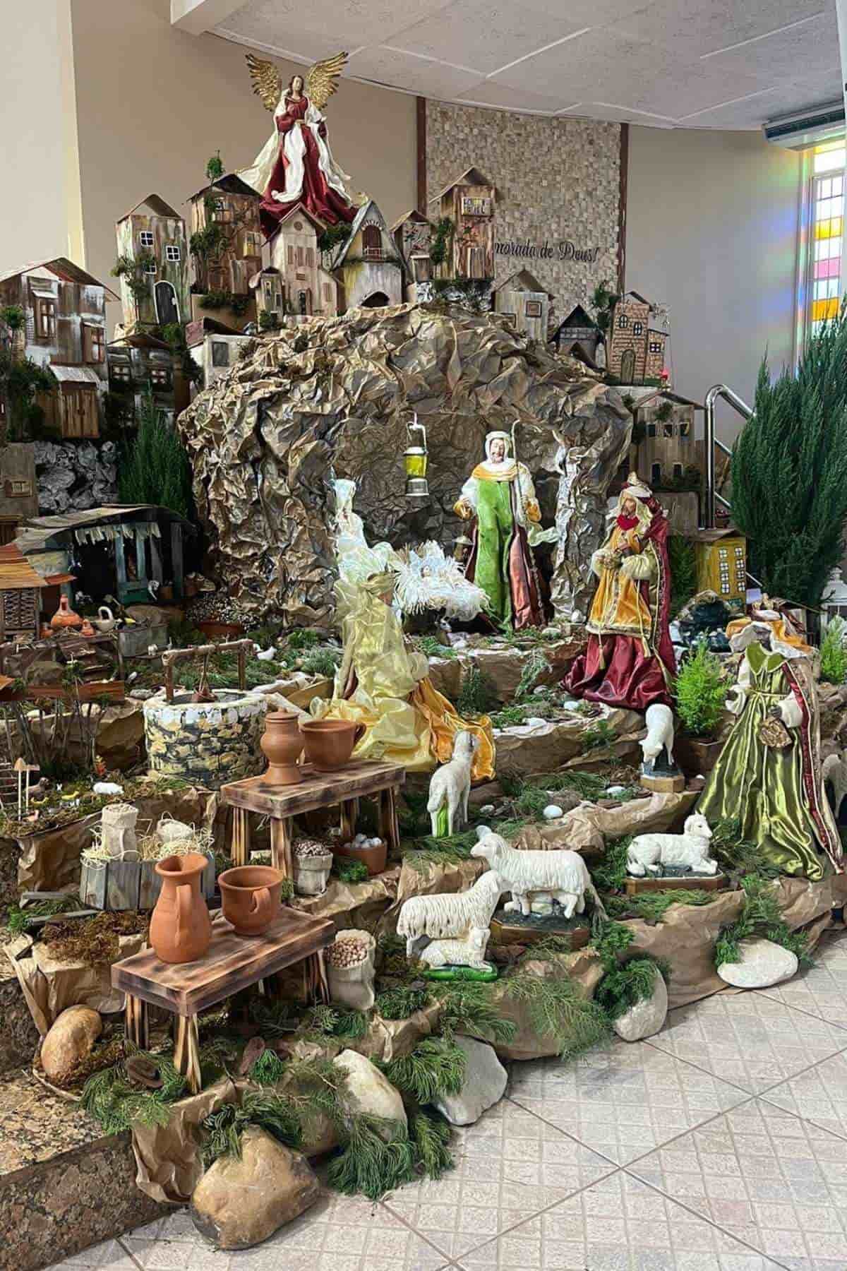 A detailed Bethlehem village with figurines of people, animals, and buildings arranged on various levels with greenery and props, depicting the birth of Jesus.