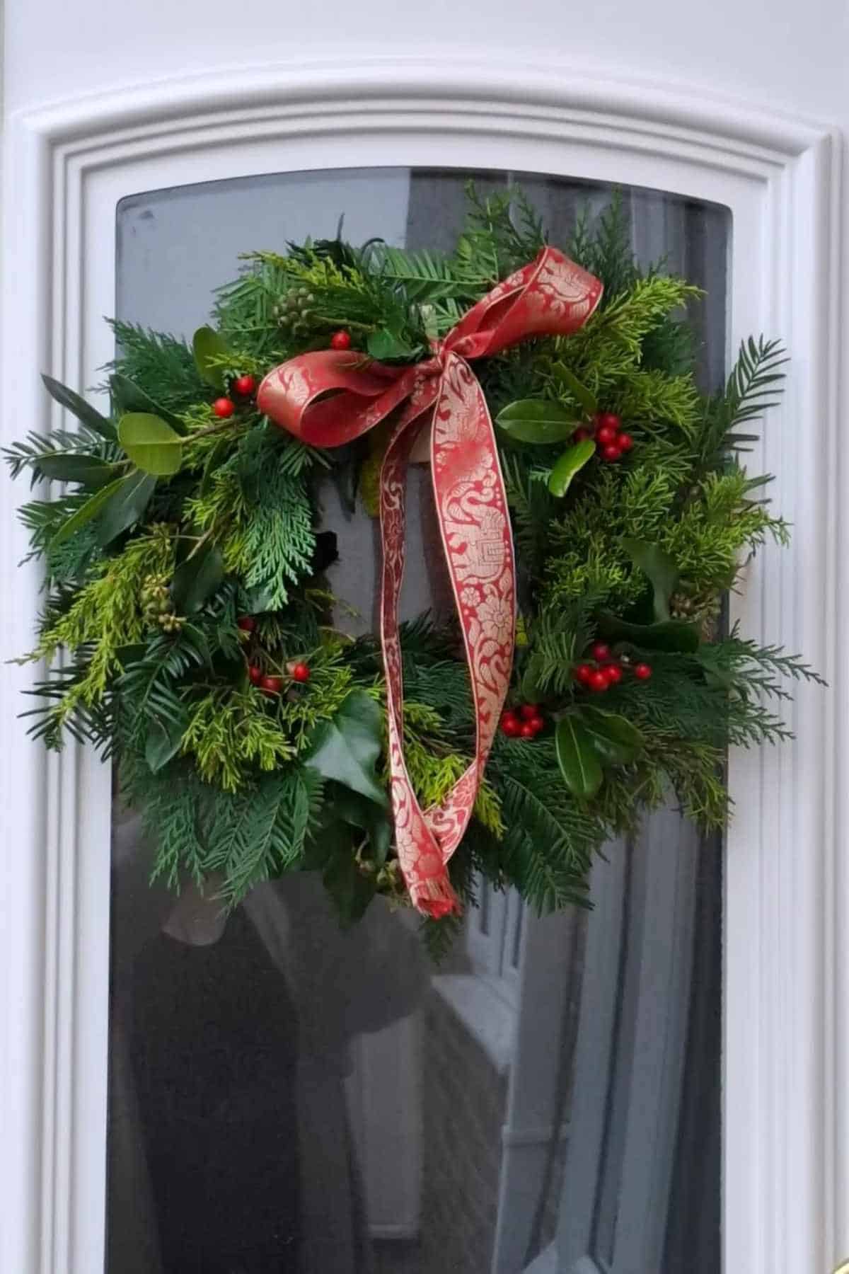 A green wreath with red berries and a red patterned ribbon hangs on a glass panel door.