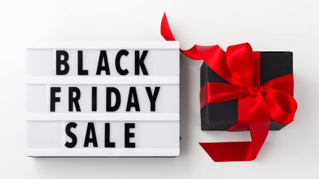 Lightbox sign with "Black Friday Sale" text next to a black gift box wrapped with a red ribbon, on a white background.