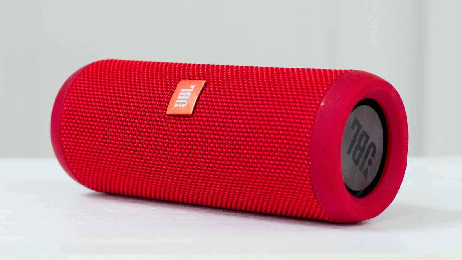A red cylindrical JBL portable Bluetooth speaker is placed on a white surface against a plain background.