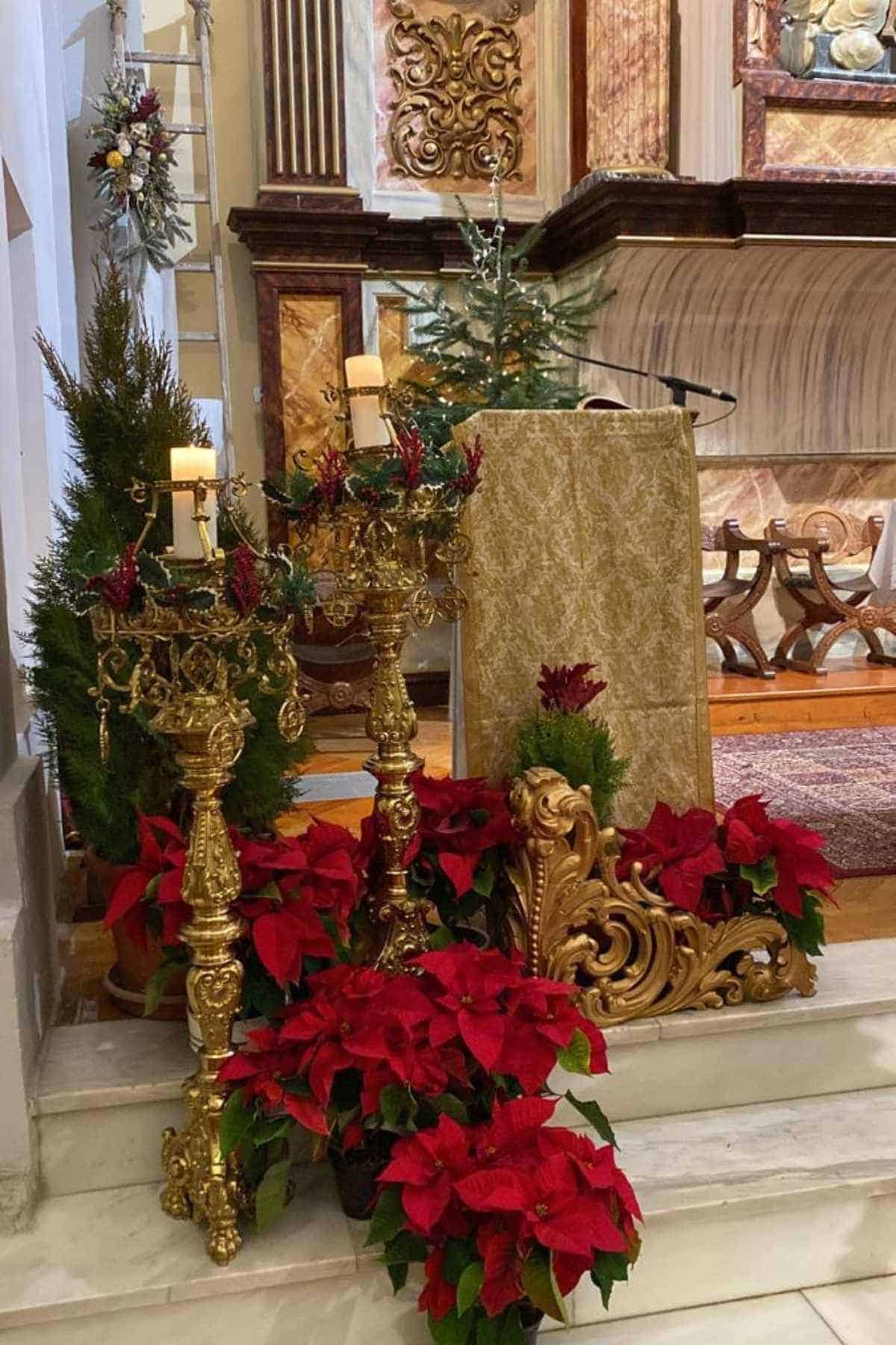 A church altar decorated with gold candlesticks, poinsettias, greenery, and a lectern, with a Christmas tree visible in the background.