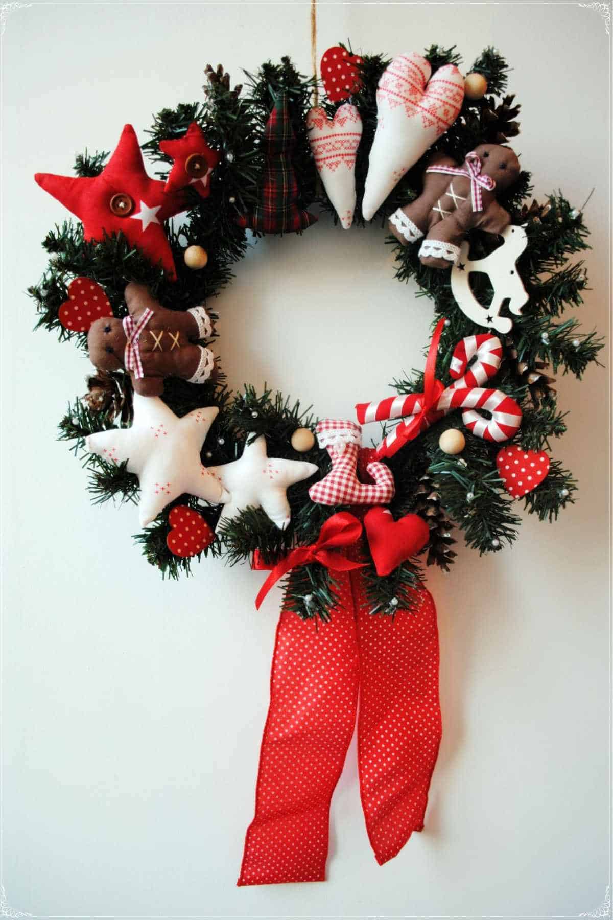 A festive wreath decorated with plush stars, hearts, gingerbread figures, candy canes, polka dot bows, and a large red ribbon at the bottom.