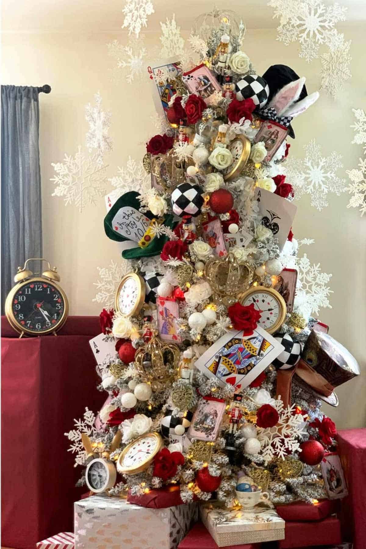 A Christmas tree decorated with large playing cards, clocks, red and white ornaments, and gold crowns, surrounded by snowflake decorations and wrapped gifts at the base.