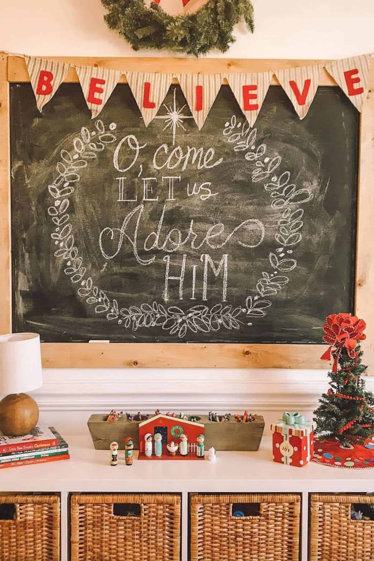 A chalkboard with "O come let us adore Him" written in script, surrounded by Christmas decor and a "BELIEVE" banner above.