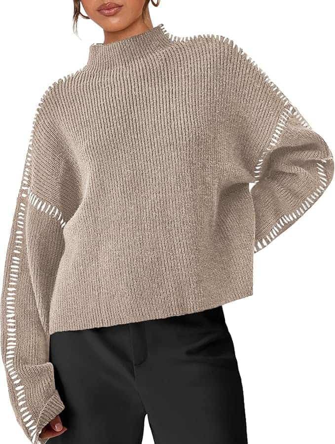 A person wearing a loose-fitting beige knit sweater with wide sleeves and black pants, shown from the shoulders down.