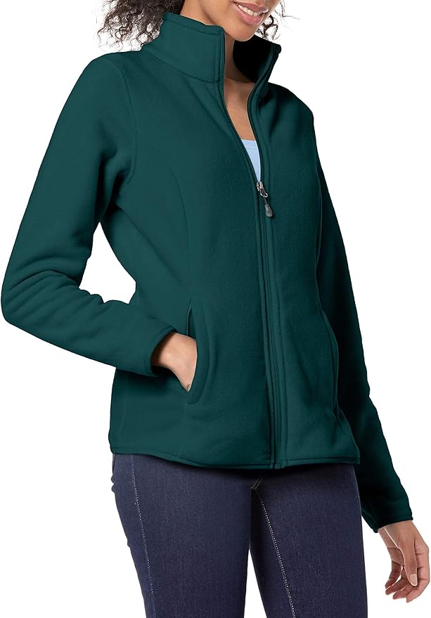 A woman wearing a dark green zip-up fleece jacket with her left hand in the pocket, paired with blue jeans.