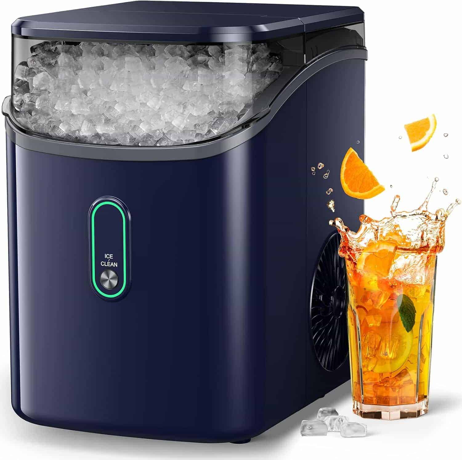 A navy blue countertop ice maker filled with ice, next to a glass of iced tea with orange slices and ice cubes scattered nearby.
