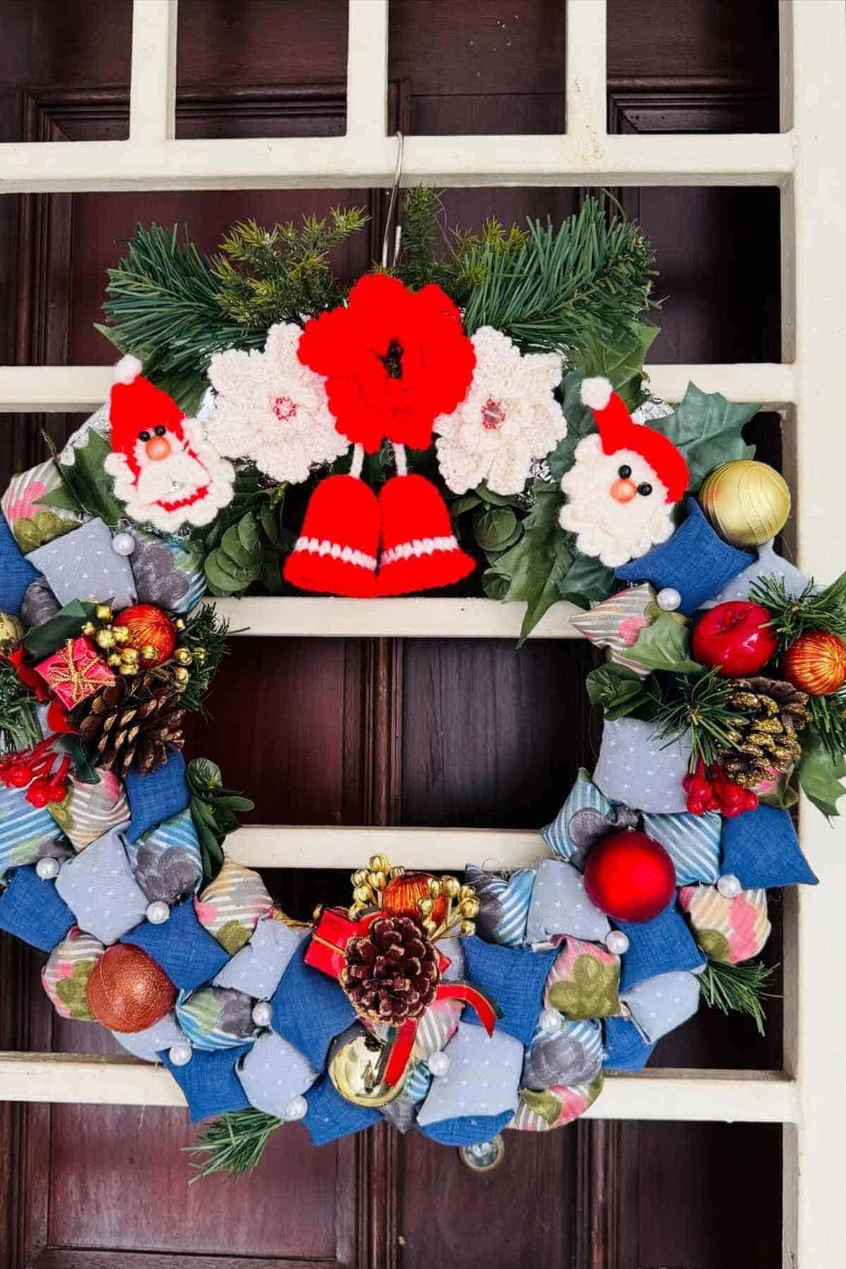 A festive wreath with pine cones, ornaments, bows, and small Santa decorations hangs on a wooden door.