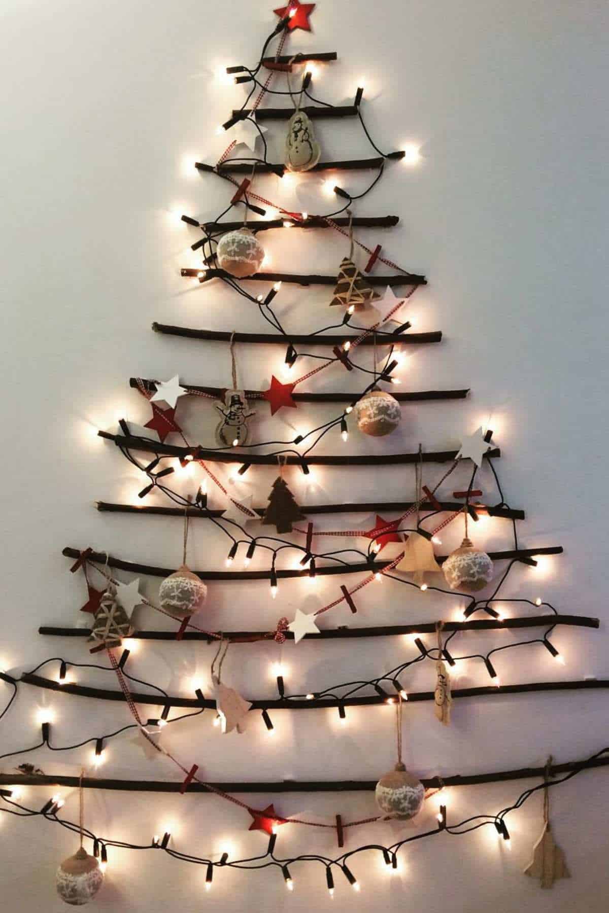 Wall-mounted Christmas tree made of horizontal sticks, decorated with string lights, ornaments, and stars.