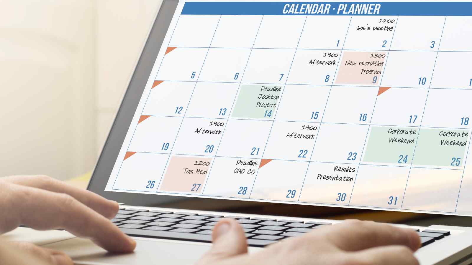 A person uses a laptop displaying a monthly calendar planner with scheduled meetings, project deadlines, and events.