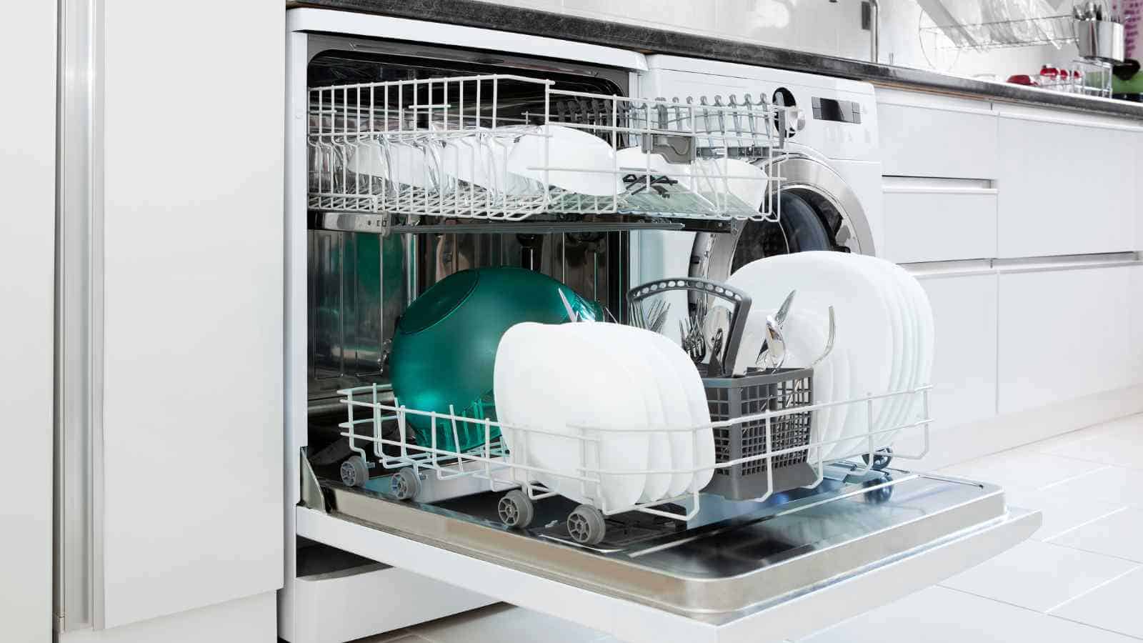 An open dishwasher with clean plates, bowls, and cutlery neatly arranged in two racks in a modern kitchen.
