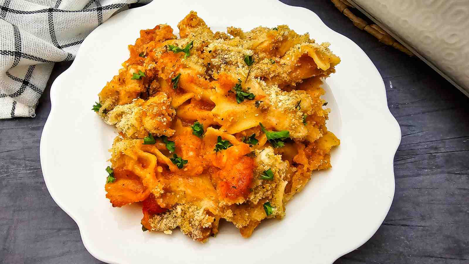 A serving of baked chicken parmesan with tomato sauce, melted cheese, breadcrumbs, and chopped parsley on a white plate.