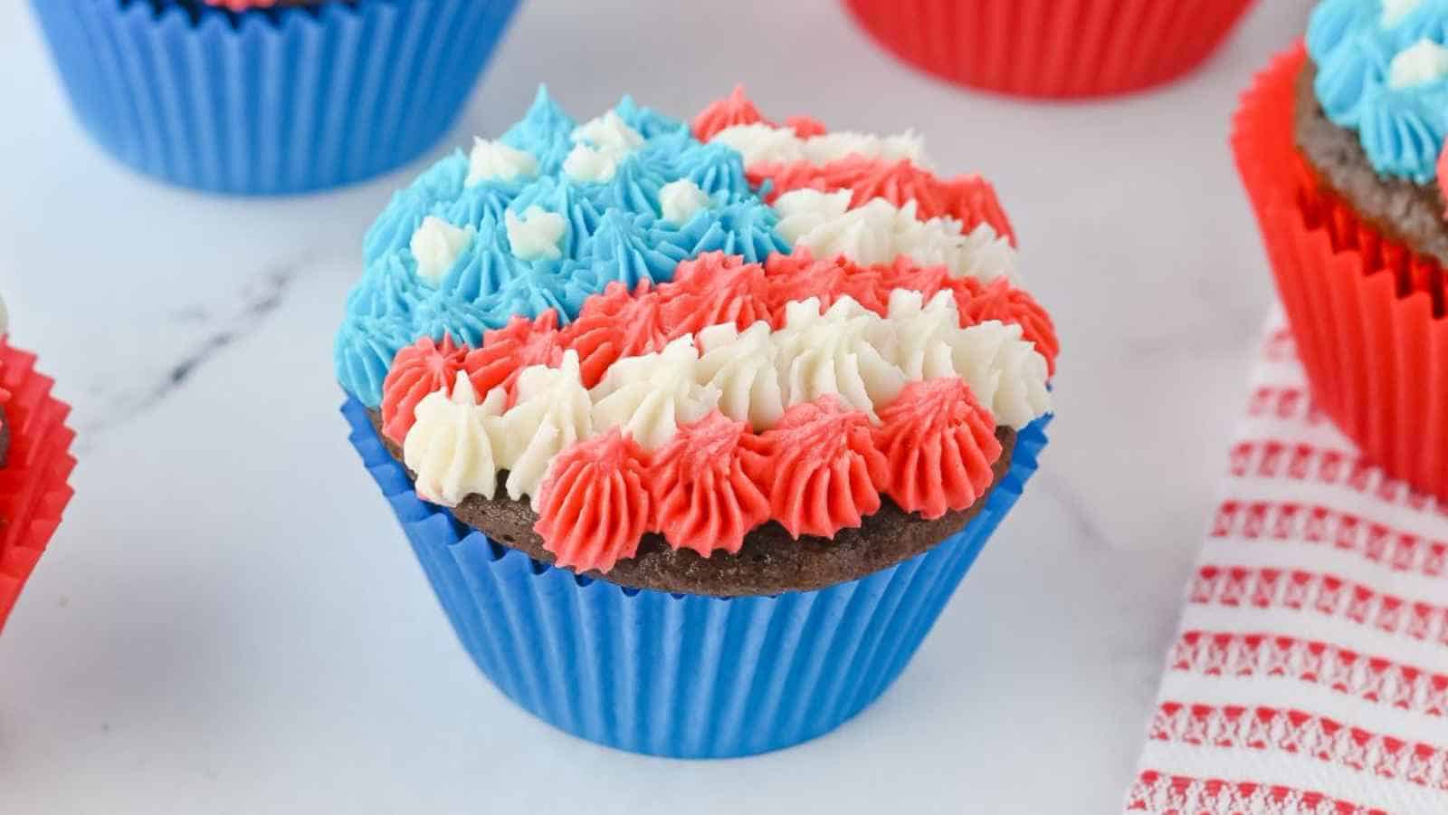 Chocolate cupcake in a blue wrapper topped with red, white, and blue striped frosting, resembling the American flag pattern.