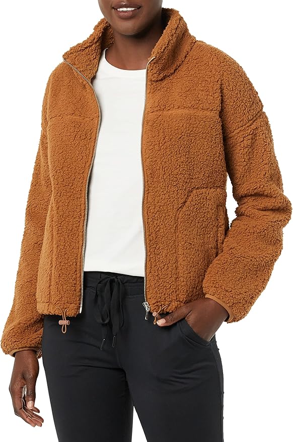 A person wearing a brown sherpa fleece zip-up jacket over a white shirt and black pants, with one hand in the jacket pocket.