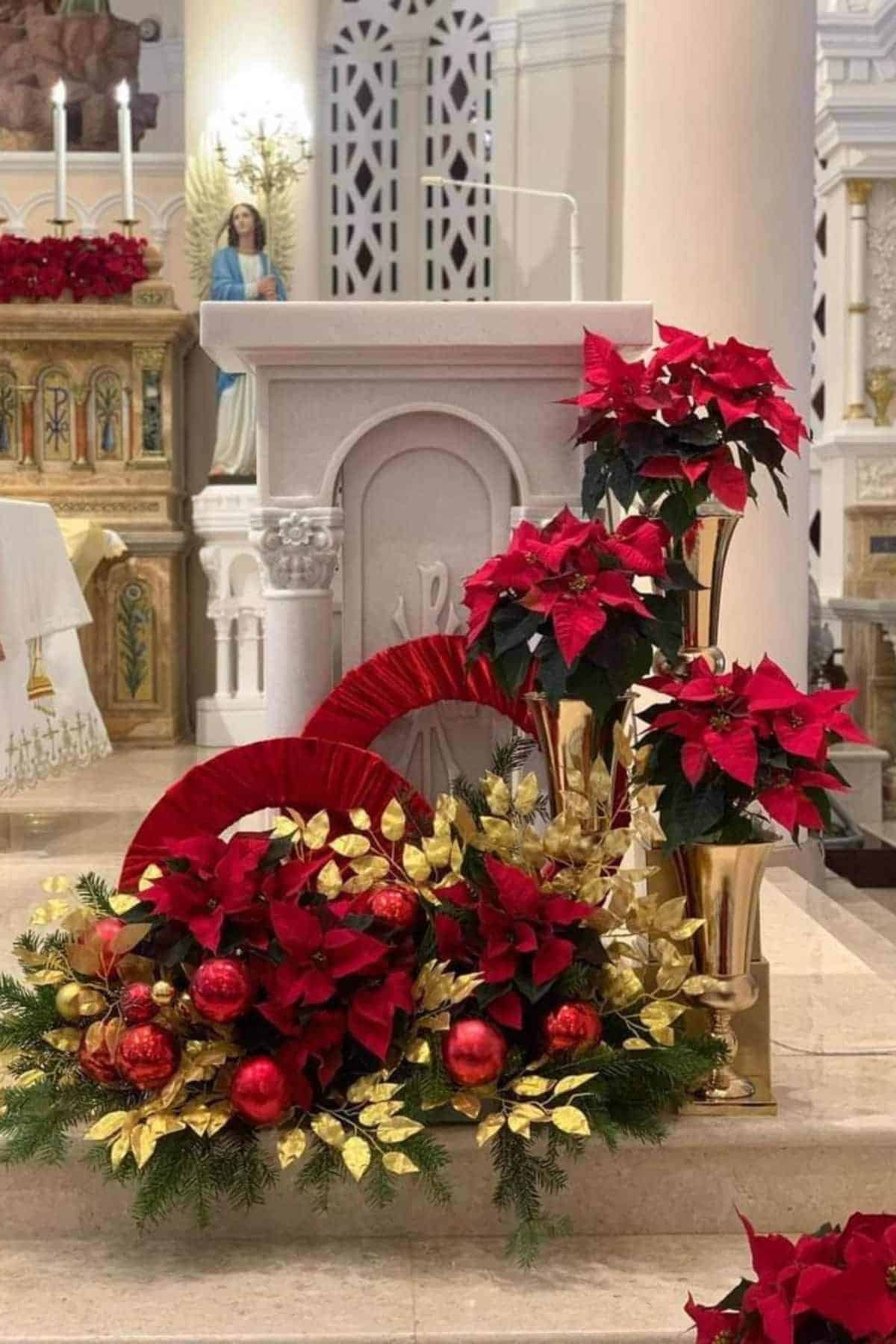 A church lectern decorated with red poinsettias, gold leaves, and red ornaments, with altar and a statue of an angel visible in the background.