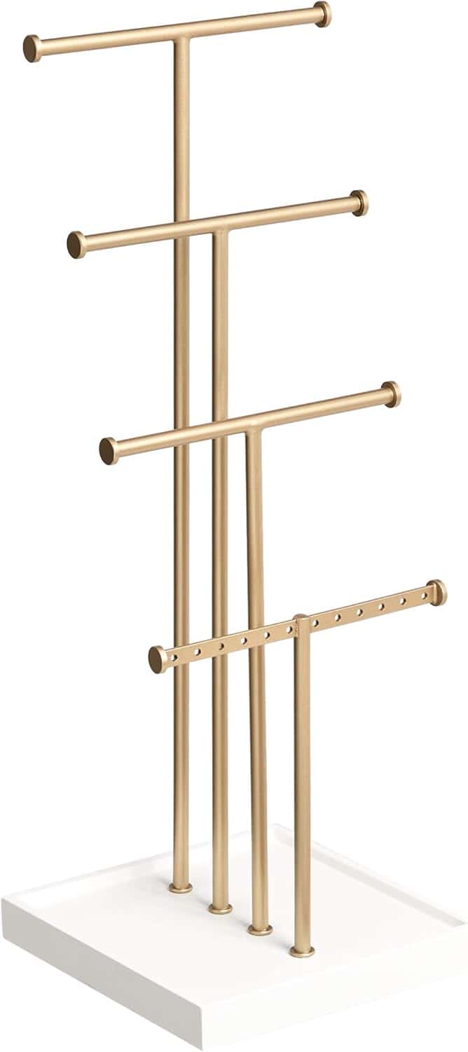 Gold metal jewelry stand with four staggered horizontal bars on a white rectangular base, designed for organizing necklaces, bracelets, and other accessories.