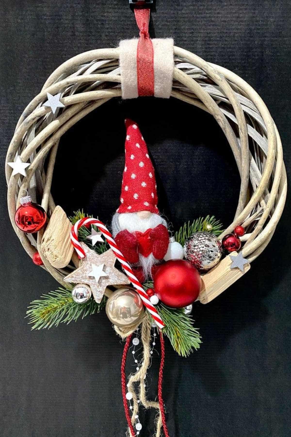A decorative Christmas wreath with a small gnome, candy cane, ornaments, stars, and greenery against a black background.