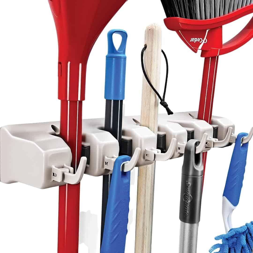 A wall-mounted organizer holds cleaning tools including a broom, mop, and dustpan, each secured in individual slots and hooks.