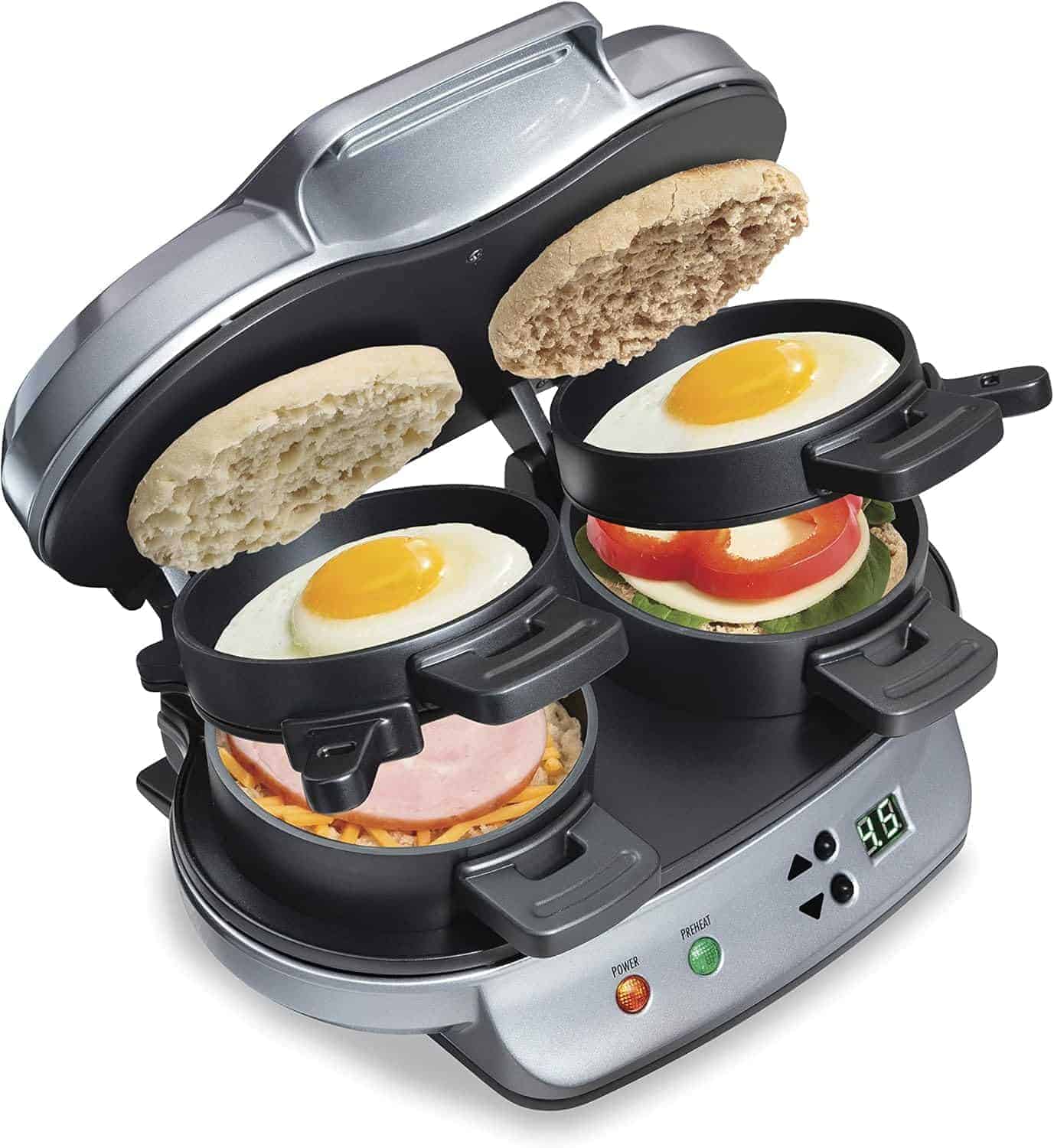 A breakfast sandwich maker with two sandwiches being cooked; each has an English muffin, egg, cheese, ham, and tomato inside individual compartments.