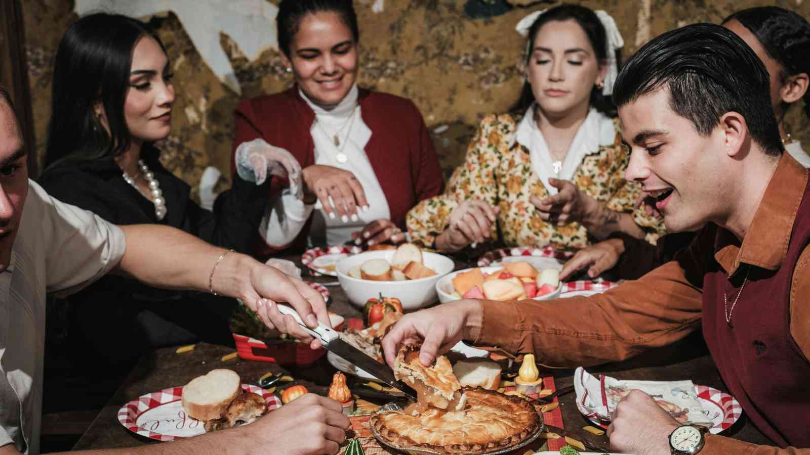 A group of people sitting around a table share food, including pie and bread, while engaging in conversation and enjoying a meal together.