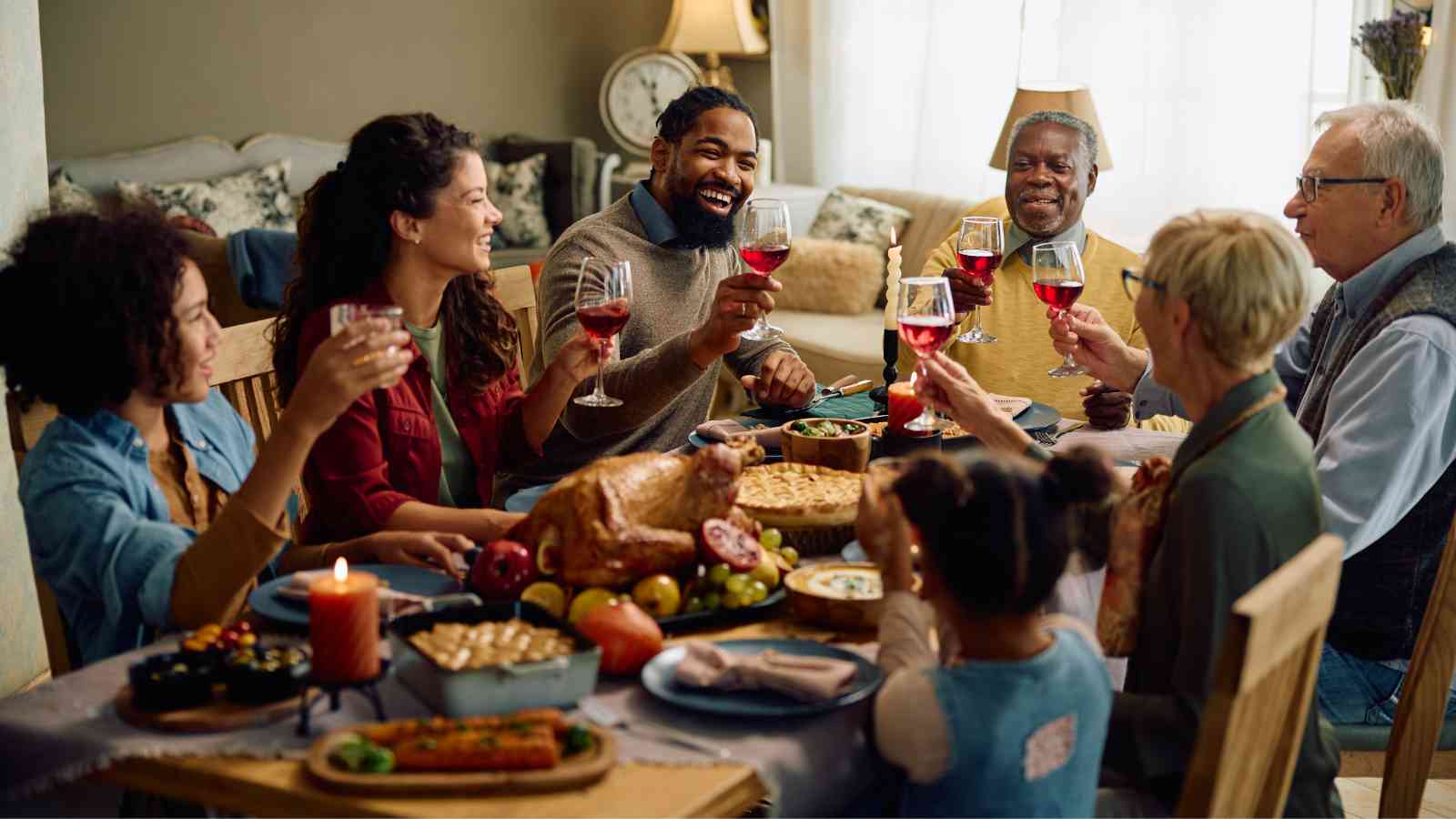 A group of people sit around a dining table, raising glasses for a toast, with various dishes and a roasted turkey in the center.