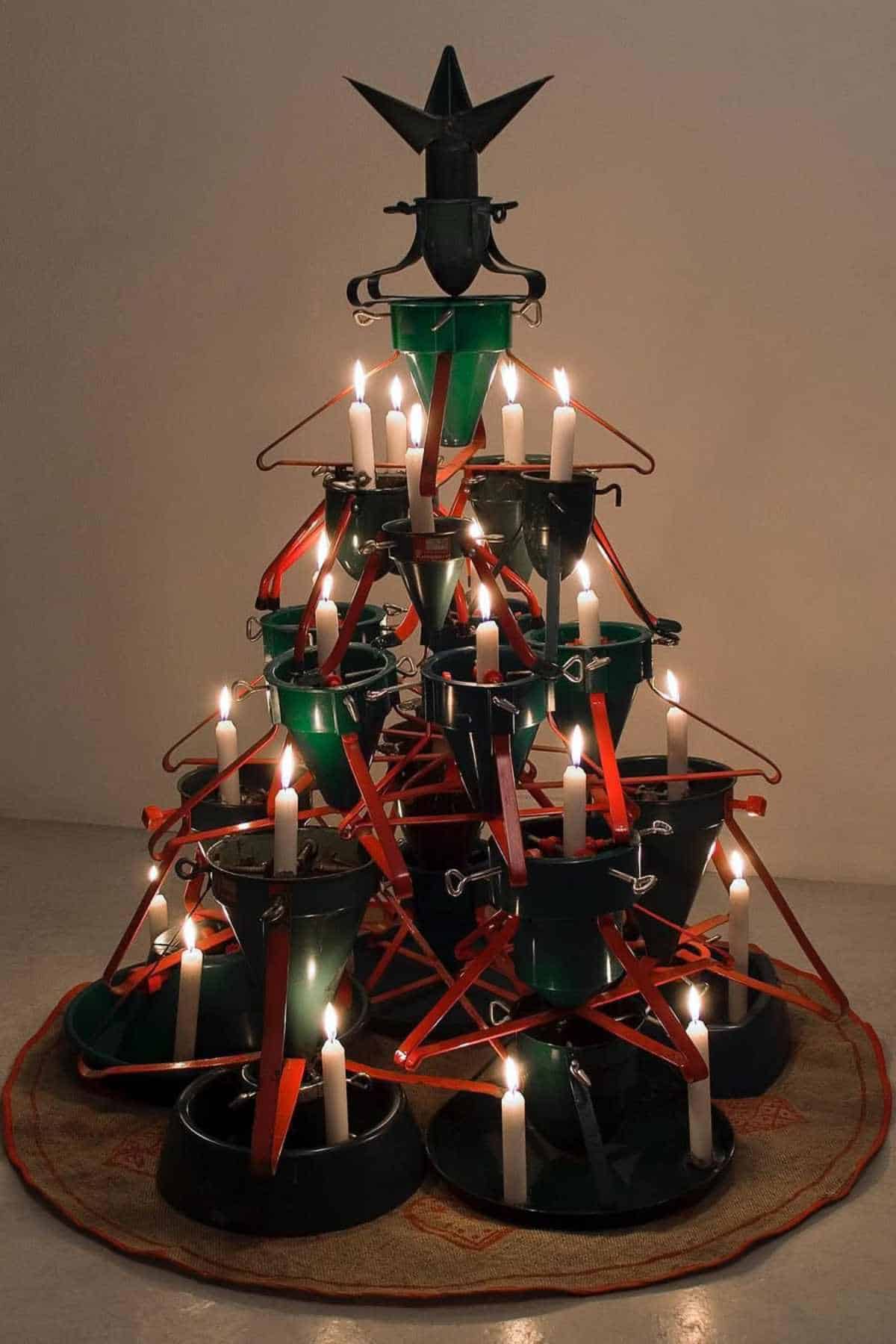 A Christmas tree sculpture made from green buckets, red hangers, and candles, arranged in a pyramid shape with a star-shaped object on top.