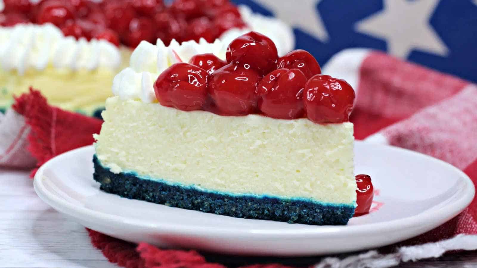 A slice of cheesecake with a blue crust, topped with whipped cream and cherry topping, on a white plate.