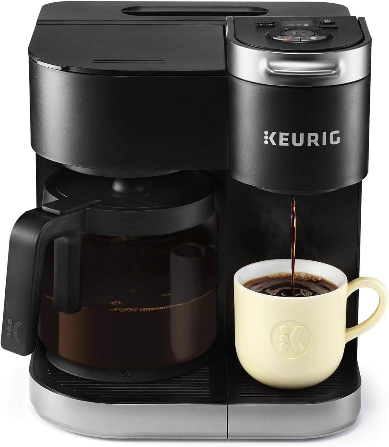 A black Keurig coffee maker brews coffee into a white mug, with a glass carafe filled with coffee positioned on the left side.