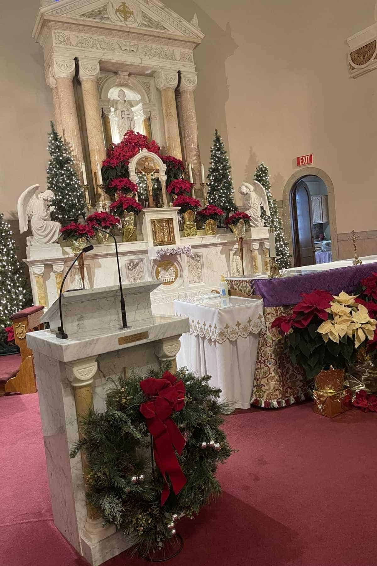Marble altar decorated with red poinsettias, Christmas trees, and festive wreaths in a church with a podium in the foreground.