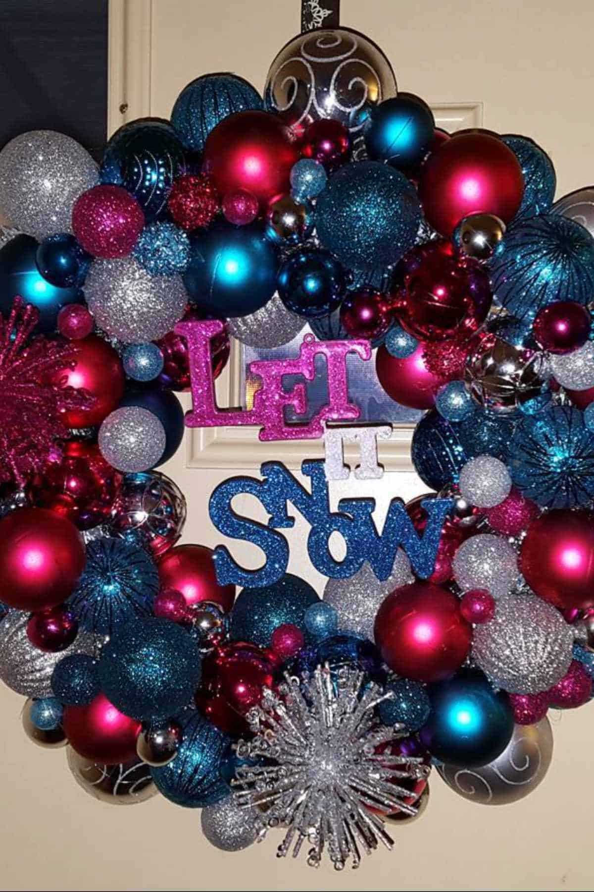 A festive wreath made of pink, blue, red, and silver ornaments with glitter accents and the words "LET IT SNOW" in the center.