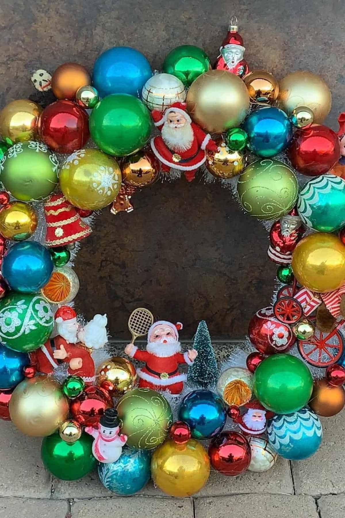 A colorful holiday wreath decorated with shiny ornaments and small Santa Claus figurines, set against a brown background.