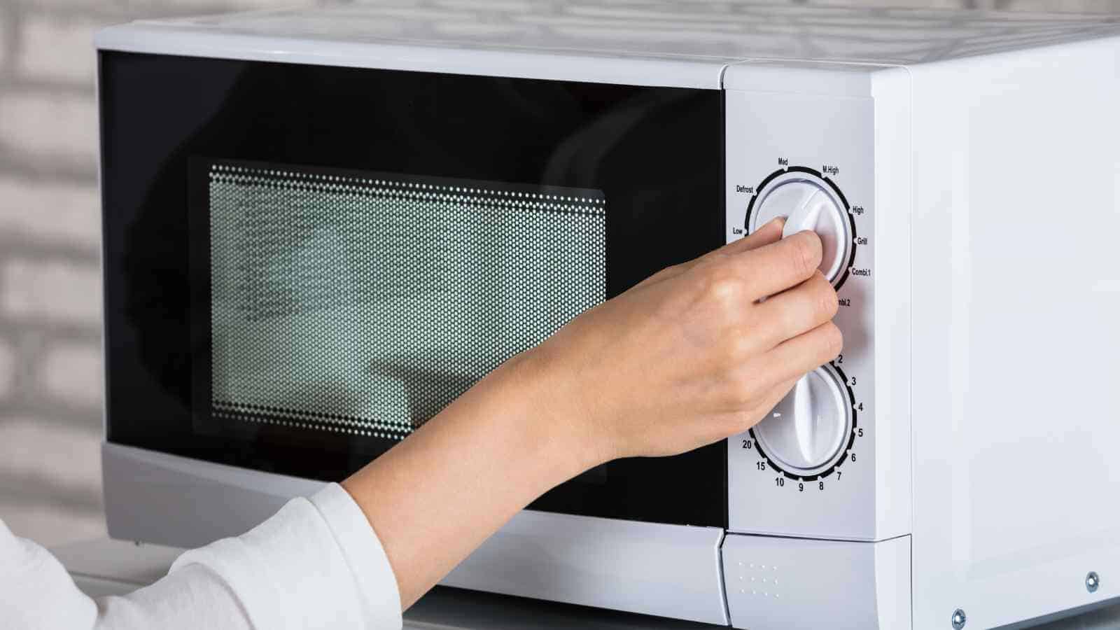A person’s hand is turning the dial on a white microwave oven.