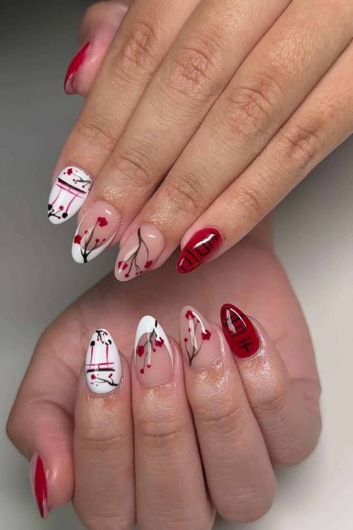 Hands with almond-shaped nails featuring red, white, and black abstract nail art, including lines, hearts, and floral designs on a light background.